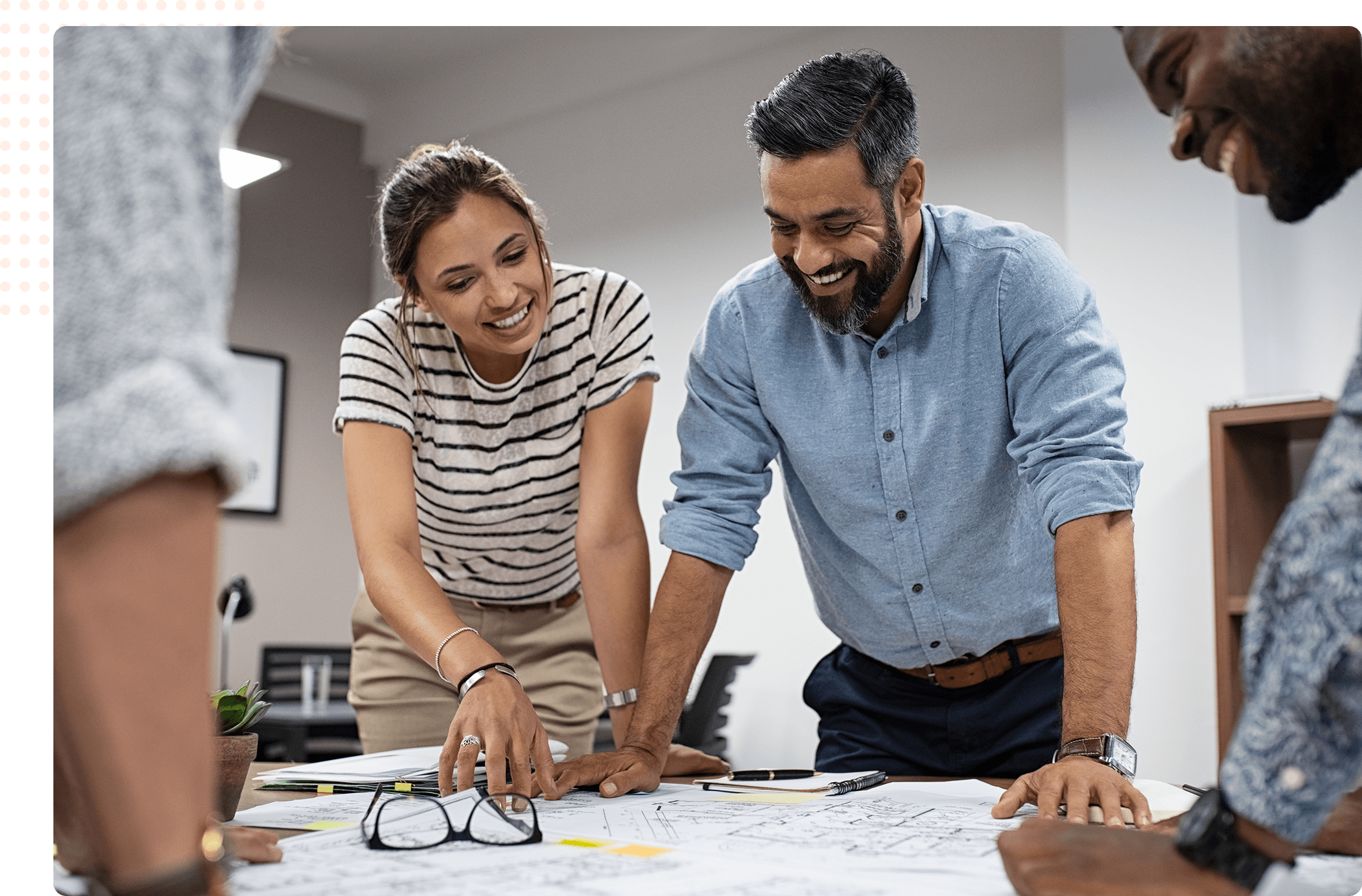Três profissionais sorridentes, uma mulher e dois homens, colaborando em um projeto ao redor de uma mesa com papéis e plantas arquitetônicas espalhados. Cuidando do seu negócio com a Hallco. 